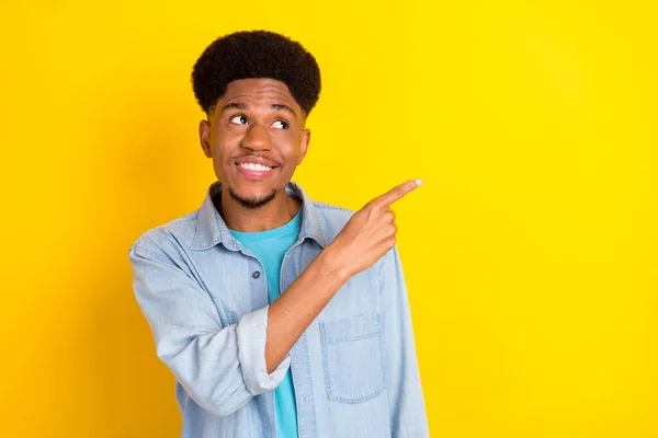 Photo of funky dreamy dark skin guy dressed denim shirt smiling looking pointing finger empty space isolated yellow color background — Foto Stock