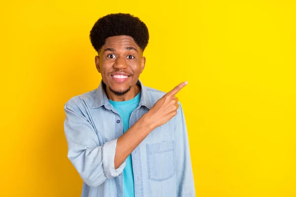 Photo of cute attractive dark skin man wear jeans shirt smiling pointing finger empty space isolated yellow color background — 图库照片