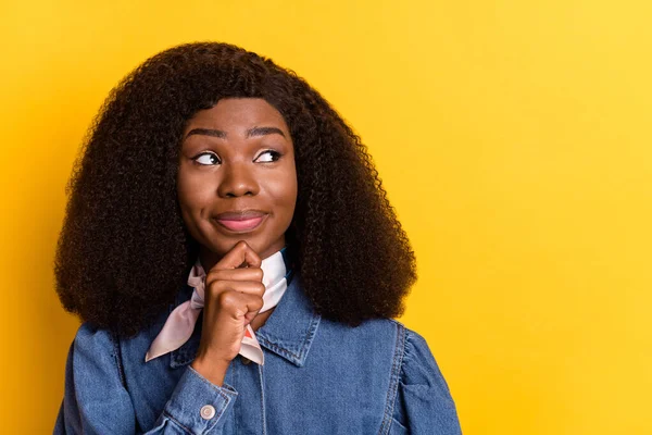 Photo of charming dark skin girl arm finger on chin look interested empty space isolated on yellow color background — стоковое фото