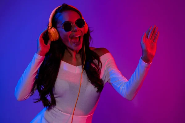 Foto de divertida dama morena hipster millennial escuchar música danza con gafas vestido blanco aislado sobre fondo colorido gradiente —  Fotos de Stock