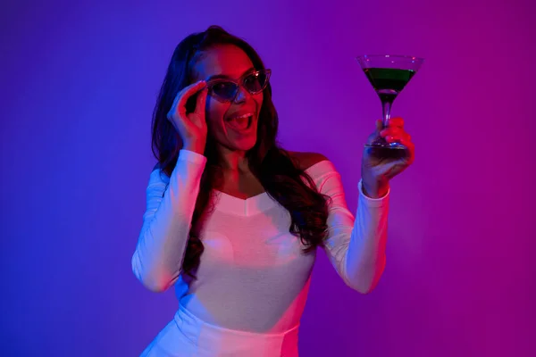 Photo of hooray young brunette lady drink alcohol wearing white dress spectacles isolated over neon colorful background — Foto Stock