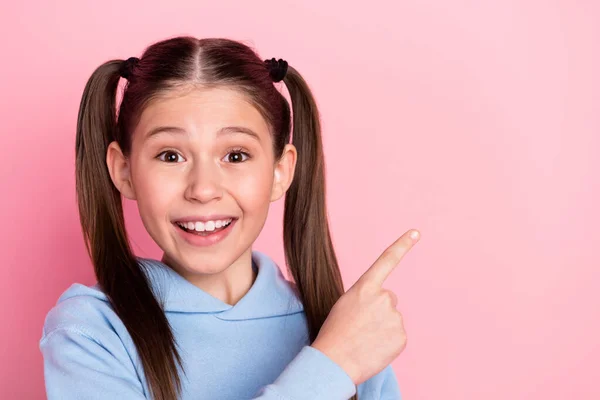Foto portrét malé školačky ukazující prstem prázdný prostor s úsměvem izolované na pastelové růžové pozadí — Stock fotografie