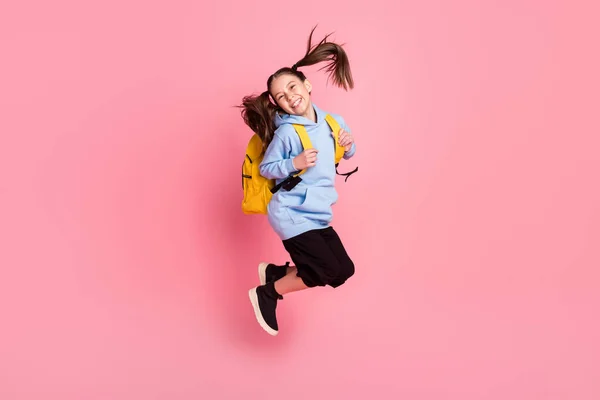 Tamanho total do corpo foto de menina saltando com mochila amarela rindo isolado pastel cor-de-rosa fundo — Fotografia de Stock
