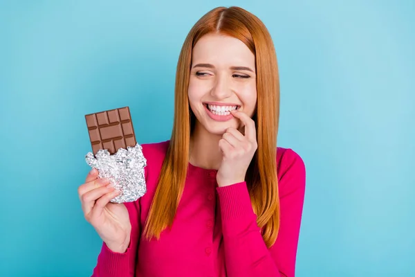 Foto van nieuwsgierig jong rood haar dame kijken chocolade dragen roze trui geïsoleerd op blauwe kleur achtergrond — Stockfoto