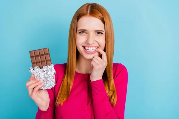 Foto van glanzende charmante jonge dame gekleed roze outfit glimlachende bijtende vinger eten chocolade geïsoleerde blauwe kleur achtergrond — Stockfoto