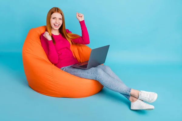 밝고 명랑 한 여자가 가방 의자에 앉아 밝은 파란색 배경에서 외롭게 있는 노트북을 사용하는 모습 — 스톡 사진