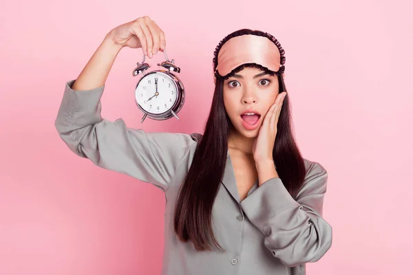 분홍색 파스텔 색 배경 위로 깨어 있는 시계를 들고 있는 아름답고 놀란 소녀의 모습 — 스톡 사진