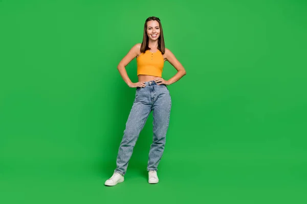 Plná délka fotografie chladné mladé brunetky dáma stojí nosit horní džíny tenisky izolované na zeleném pozadí — Stock fotografie