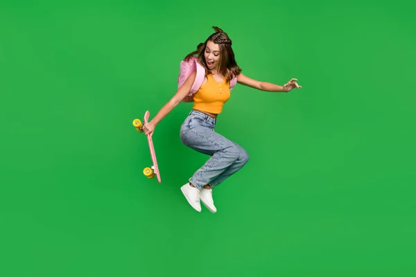 Foto de comprimento total de jovens engraçado morena senhora segurar skate salto desgaste top jeans saco sapatos isolados no fundo verde — Fotografia de Stock