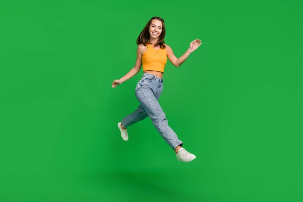 Foto de tamaño completo de la joven morena agradable señora correr usar top jeans zapatos aislados sobre fondo verde —  Fotos de Stock