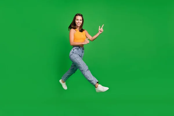 Foto de longitud completa de millennial divertida señora morena punto de ejecución llevar top jeans zapatos aislados sobre fondo verde — Foto de Stock