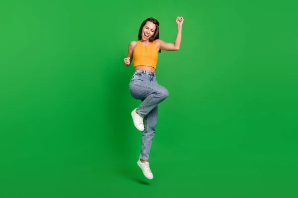 Full size photo of young hooray brunette lady jump wear top jeans shoes isolated on green background — Fotografia de Stock