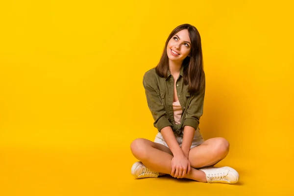 Photo of dreamy lady sit floor look empty space wear green shirt mini skirt sneakers isolated yellow color background.
