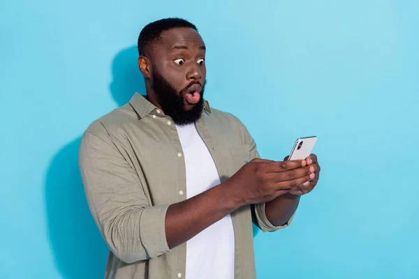 Profil côté photo de jeune homme africain impressionné utiliser smartphone nouvelles omg commentaire isolé sur fond de couleur bleue — Photo
