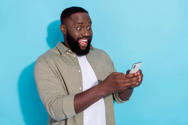 Profil photo de côté de jeune homme africain excité utiliser le partage de téléphone portable app télécharger isolé sur fond de couleur bleue — Photo