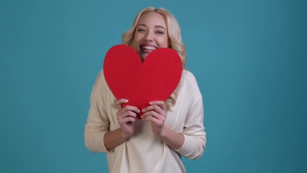 Atractiva dama sostiene el puño del corazón de la postal hasta fondo azul aislado — Vídeos de Stock