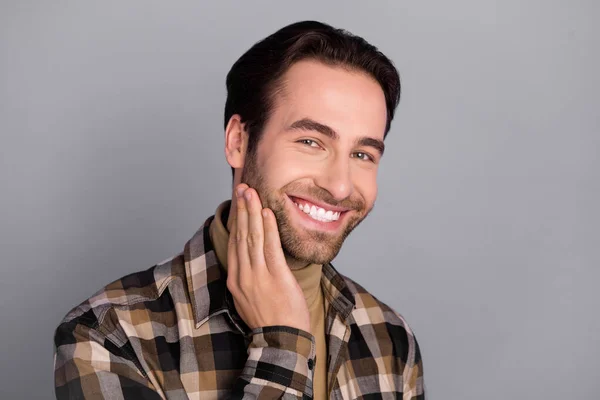 Portrait of attractive well-groomed cheerful guy wearing checked shirt touching face beard isolated over grey color background — Stockfoto
