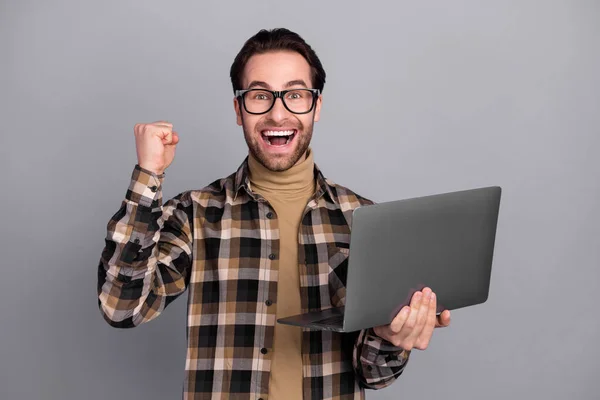 Photo of cheerful lucky man wear plaid shirt spectacles rising fist holding gadget isolated grey color background — Φωτογραφία Αρχείου