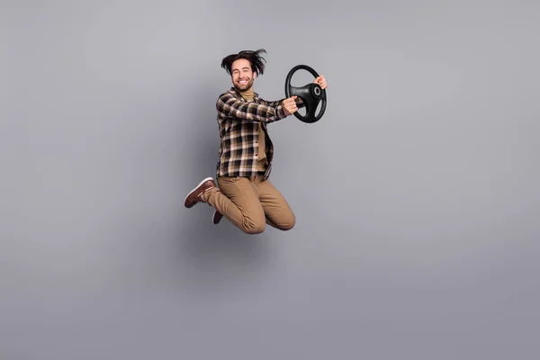 フル長ボディサイズビューの魅力的な陽気な男ジャンプ保持ステアリングホイール絶縁以上グレー色の背景 — ストック写真