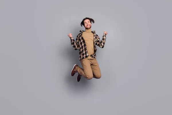 Bilde av sjarmerende heldig mann med rutete skjorte som hopper høyt opp knyttnever isolert grå fargebakgrunn – stockfoto