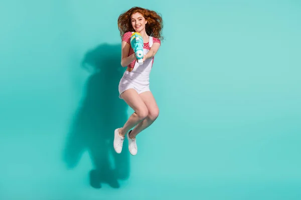 フル長いボディサイズビューの魅力的なトレンディーな陽気な女の子ジャンプ使用して銃おもちゃ孤立した明るい青の色の背景 — ストック写真