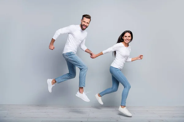 全长照片 让人印象深刻的年轻黑发夫妇穿着灰色背景的白衬衫牛仔裤运动鞋跑步 — 图库照片