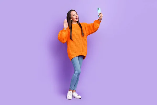 Foto av roliga vackra dam håll telefonen ta selfie våg hand bära orange pullover isolerad violett färg bakgrund — Stockfoto