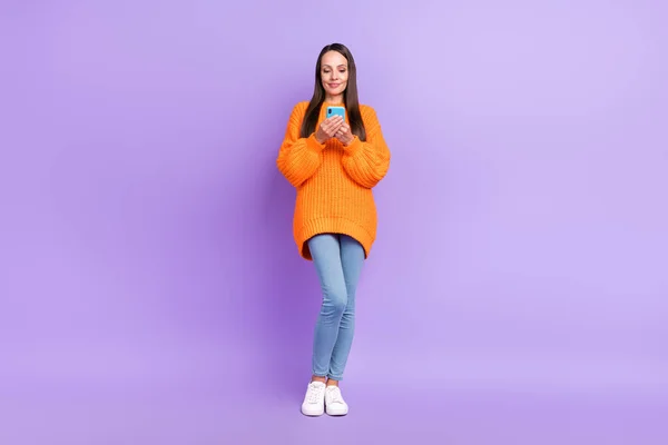 Foto av glada bloggare dam hålla telefon chat vänner bära orange tröja jeans isolerad violett färg bakgrund — Stockfoto