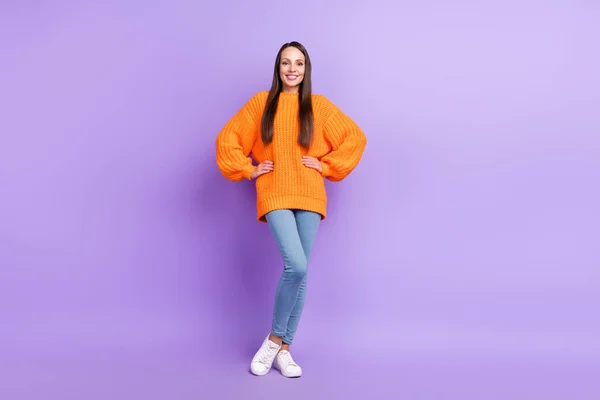 Zdjęcie wesołe ładna dziewczyna pani pozowanie ręce biodra nosić pomarańczowy pullover odizolowany fioletowy kolor tła — Zdjęcie stockowe