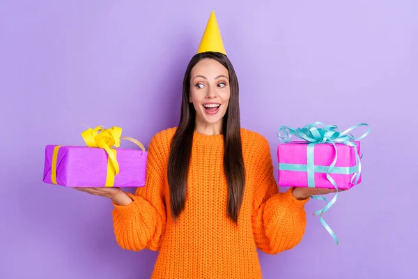Photo of excited surprised lady hold two presents make choice wear cone cap orange sweater isolated purple color background — Stok fotoğraf