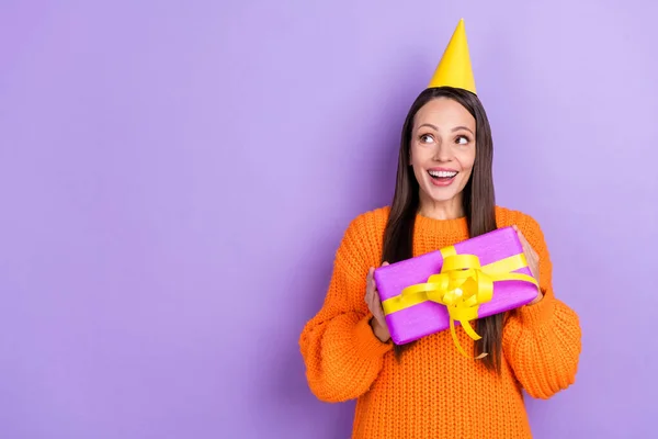 Фото веселой мечтательной леди держать подарок предвидеть исполнение желания носить оранжевый свитер изолированный фиолетовый цвет фона — стоковое фото