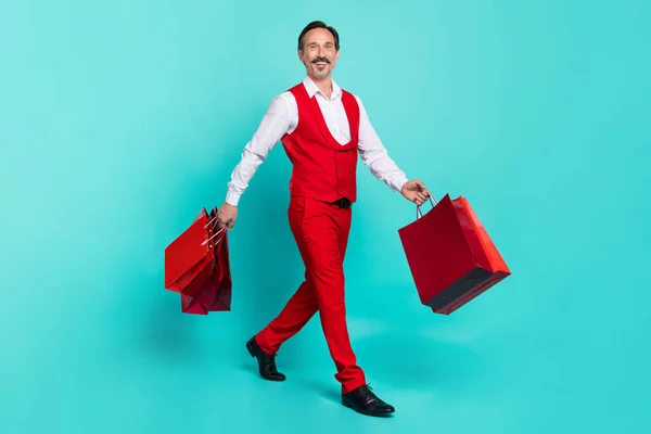 Full body profile side photo of aged man go hold shopping bags boutique delivery isolated over teal color background — стоковое фото