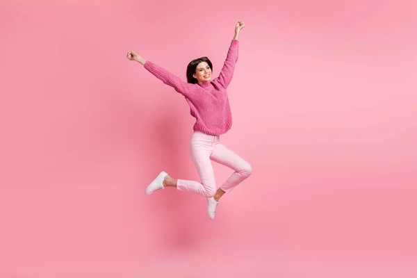 フルサイズ写真のブルネット面白い女の子ジャンプ着用ピンクセーターパンツスニーカー絶縁上の真紅の背景 — ストック写真