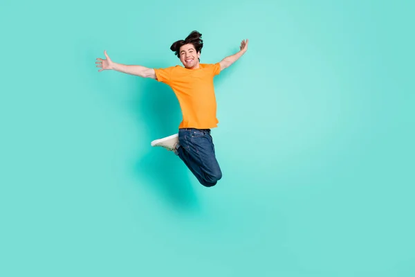 フルサイズ写真の面白い茶色の髪若い男ジャンプ着用Tシャツジーンズスニーカー隔離された青の背景 — ストック写真