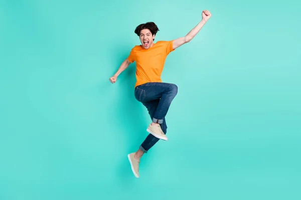 フルサイズ写真の面白い茶色の髪ミレニアル男ジャンプ着用Tシャツジーンズスニーカー隔離された青の背景 — ストック写真