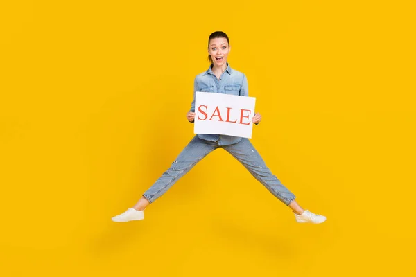 Full length body size photo smiling girl jumping up keeping sale table overjoyed isolated vivid yellow color background — Stock Fotó