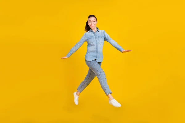 Full length photo of cute excited young woman wear denim shirt smiling jumping high isolated yellow color background — Fotografia de Stock