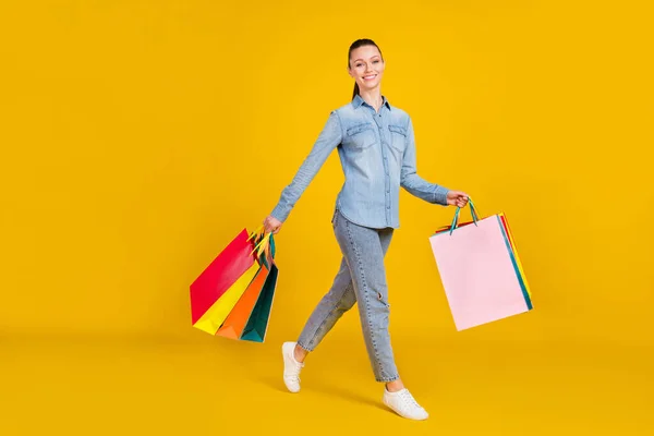 Full length photo of pretty shiny young lady dressed jeans shirt walking shopping smiling isolated yellow color background — Stockfoto