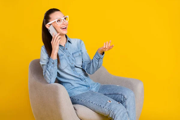 Photo portrait woman sitting in chair talking on cellphone looking copyspace isolated vibrant yellow color background — Zdjęcie stockowe