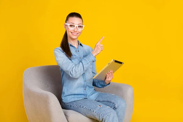 Photo of adorable sweet woman wear denim shirt glasses chair holding modern gadget empty space isolated yellow color background — Stok fotoğraf