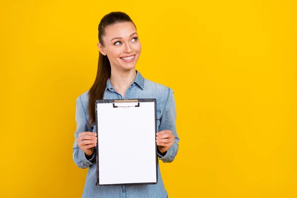 Photo of charming cute woman wear denim shirt smiling looking empty space holding clipboard isolated yellow color background — Fotografia de Stock