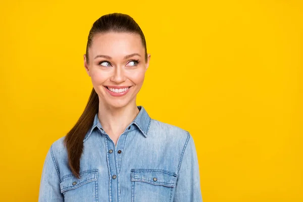 Photo of adorable sweet young lady dressed jeans shirt smiling looking empty space isolated yellow color background — Stock Fotó