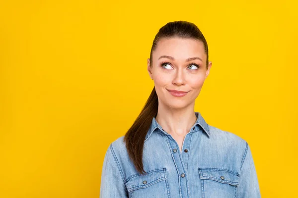Photo of dreamy adorable young lady dressed jeans shirt smiling looking empty space isolated yellow color background — 图库照片