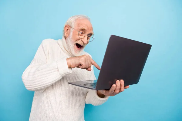 Foto de hombre de barba envejecida impresionado tipo portátil usar gafas suéter aislado sobre fondo de color azul — Foto de Stock