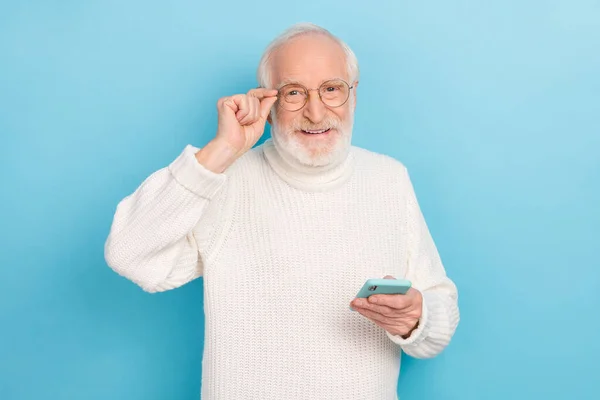 Photo of nice elder beard man hold telephone wear eyewear white turtleneck isolated on blue color background — Stok fotoğraf