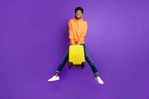 Full size photo of young black man happy positive smile jump hold suitcase travel vacation isolated over violet color background — Stok fotoğraf