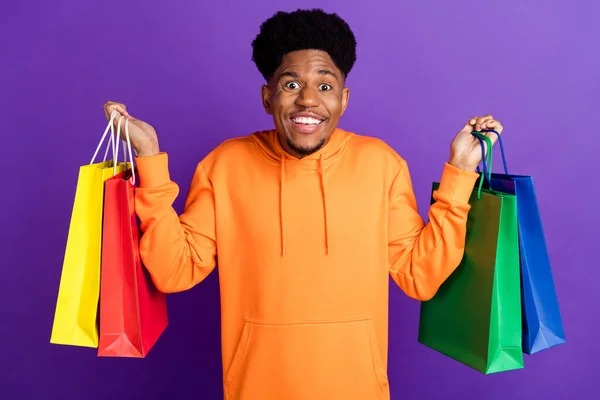 Fotografie mladého černocha šťastný pozitivní úsměv držet nákupní tašky černá pátek zákazník izolované přes fialové barvy pozadí — Stock fotografie