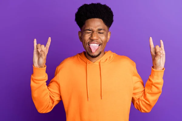 Foto de encantador joven afro americano feliz mostrar dedos signos de roca sobresalen lengua aislada sobre fondo de color púrpura —  Fotos de Stock