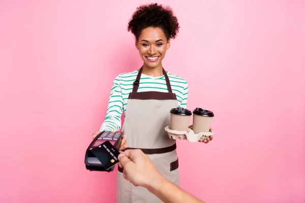 Foto de buena chica positiva mantenga café nfc aparato pago mano desgaste delantal aislado color rosa fondo —  Fotos de Stock