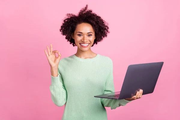 Portret van charmante vrolijke donkere huid persoon houden netbook vingers tonen okey geïsoleerd op roze kleur achtergrond — Stockfoto
